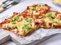 Pyszna pizza na spodzie z kalafiora keto, z szynką i serem, udekorowana świeżą pietruszką.
