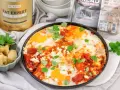 Pyszne śniadanie low carb: jajka sadzone w sosie pomidorowym z fetą i ziołami, obok pieczone karczochy. Obok produkty BE KETO.