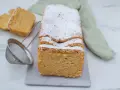 Puszyste keto ciasto z mikrofali, posypane cukrem pudrem, prezentuje się apetycznie. Obok leżą dwa kawałki ciasta i sitko.