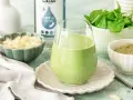 Szklanka zielonego koktajlu keto, obok miseczki ze szpinakiem, płatkami migdałów i proszkiem.