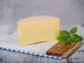 Kawałek żółtego sera, idealny na keto, z gałązką bazylii na drewnianej deseczce.