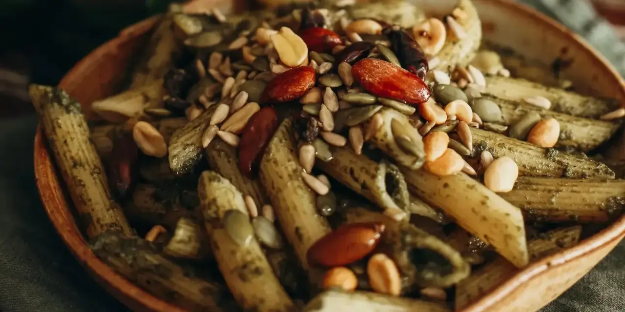 Makaron penne z zielonym pesto, posypany pestkami dyni, słonecznika, migdałami i orzeszkami ziemnymi. Idealny na dietę braci rodzeń.
