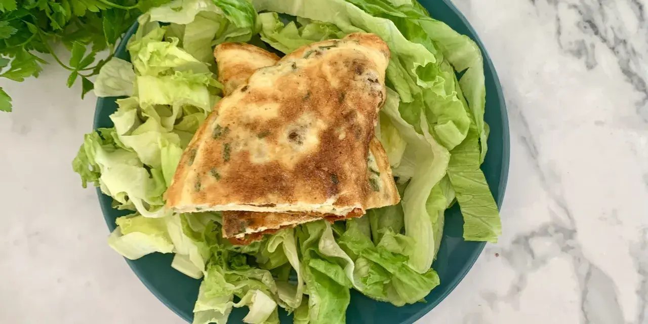 Puszysty omlet z ziołami na talerzu z sałatą.