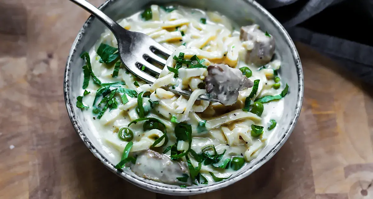 Keto makaron w kremowym sosie z groszkiem i mięsem, nabierany widelcem.