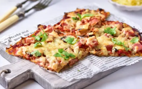 Pyszna pizza na spodzie z kalafiora keto, z szynką i serem, udekorowana świeżą pietruszką.