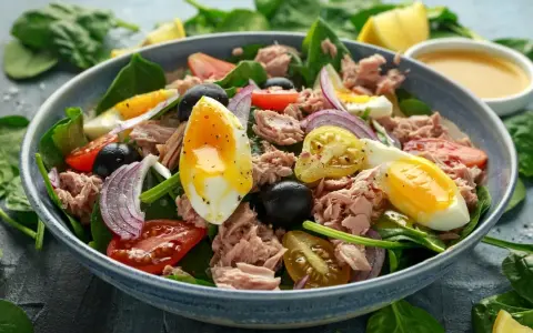 Pyszna keto sałatka z tuńczykiem, jajkiem na miękko, pomidorkami, oliwkami i czerwoną cebulą na świeżym szpinaku.