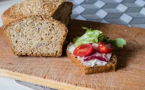 Keto chleb majonezowy przepis: kromka z serkiem, pomidorkami i sałatą obok bochenka z ziarnami.