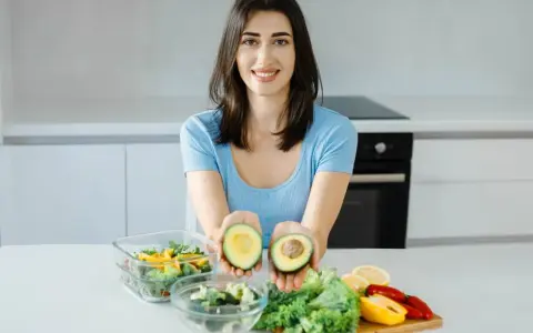 Uśmiechnięta kobieta prezentuje awokado, składnik wielu diet, w tym keto. Jej opinie o keto diecie są pozytywne.