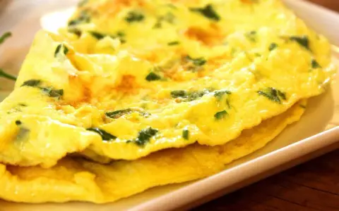 Złożony omlet z zielonymi ziołami na białym talerzu.