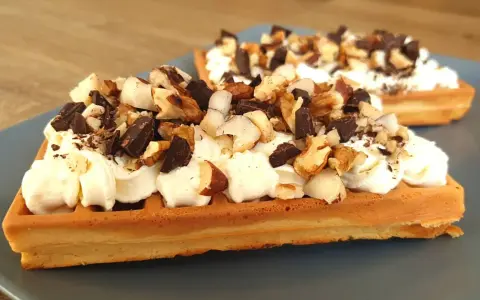 Dwa keto gofry z mascarpone, udekorowane kawałkami czekolady i orzechów. Idealne na deser.