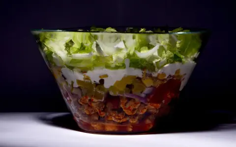 Warstwowa sałatka gyros w szklanej misie, z kurczakiem, warzywami i sosem.