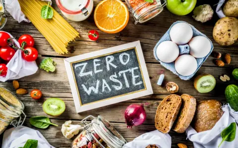 Tablica z napisem "ZERO WASTE" otoczona świeżymi warzywami, owocami, jajkami i produktami sypkimi. Styl życia bez marnowania.
