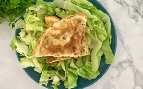 Puszysty omlet z ziołami na talerzu z sałatą.