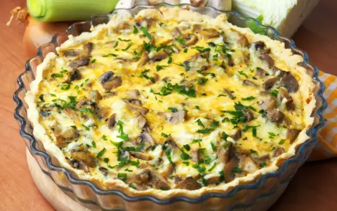 Pyszny quiche z pieczarkami, posypany świeżą natką pietruszki, w szklanej formie.
