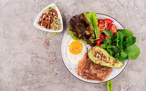 Śniadanie LCHF: jajko sadzone, boczek, awokado, sałatka z truskawkami i orzechy. Idealne na początek dnia, gdy zastanawiasz się lchf co to.