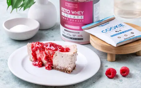 Pyszny sernik keto z malinami, obok słoik Keto Whey Isolate i batonik Keto Cookie. Idealny keto spod do sernika.