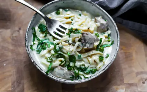 Keto makaron w kremowym sosie z groszkiem i mięsem, nabierany widelcem.