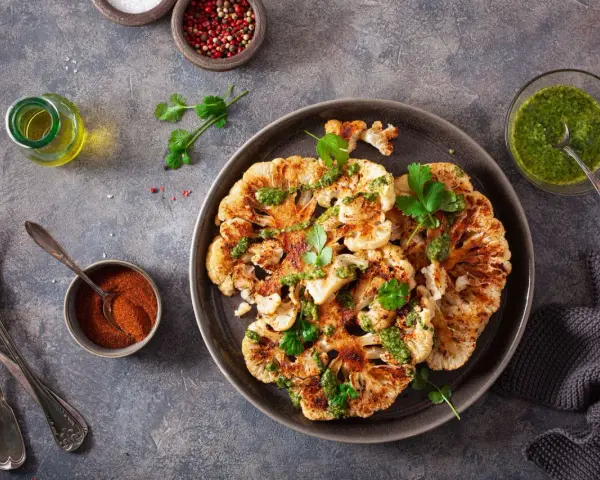Pieczony kalafior z zielonym sosem, idealny na dietę keto wege. Obok przyprawy i oliwa.