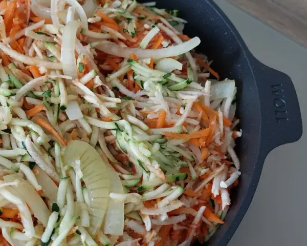 Start przygotowania keto ryby po grecku: starta marchewka, cukinia i cebula w naczyniu.