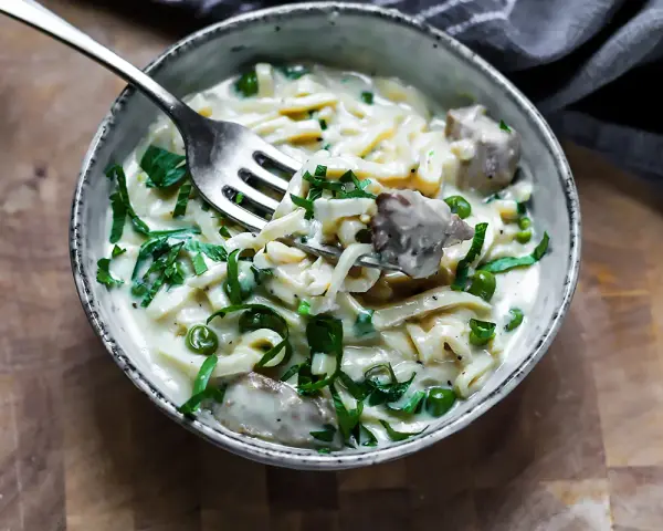 Keto makaron w kremowym sosie z groszkiem i mięsem, nabierany widelcem.