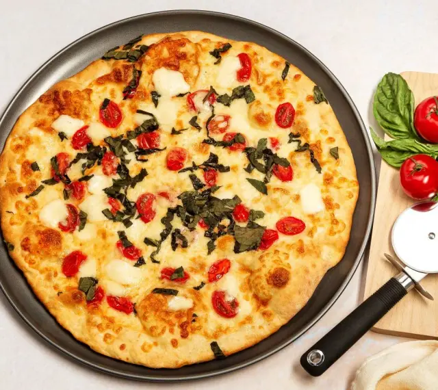 Pyszna pizza z serka wiejskiego, pomidorkami koktajlowymi i bazylią. Idealna na szybki obiad.