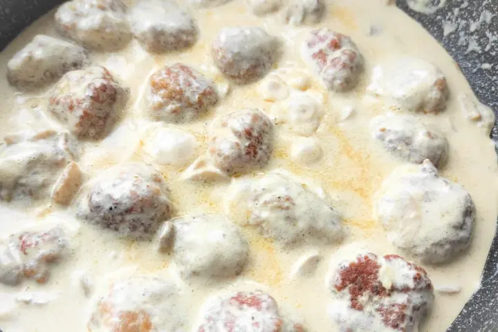 Pyszne klopsiki w sosie śmietanowym, gotujące się na patelni. Aromatyczne danie, które zachwyci każdego.