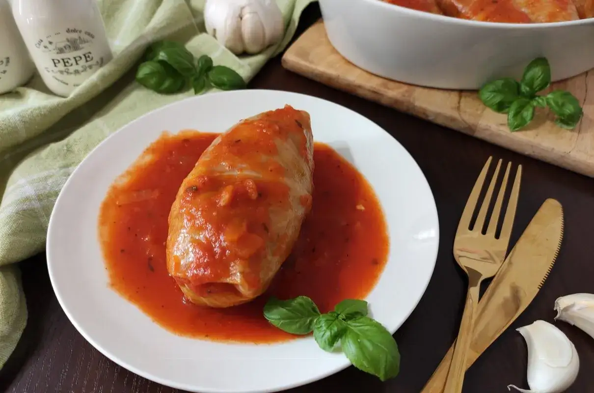 Gołąbek w sosie pomidorowym na talerzu, obok czosnek i bazylia. Zastanawiasz się, ile kcal mają gołąbki w sosie pomidorowym?