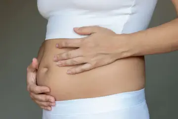 Dłońmi obejmuje zaokrąglony, napięty brzuch, który wygląda jak wzdęty.